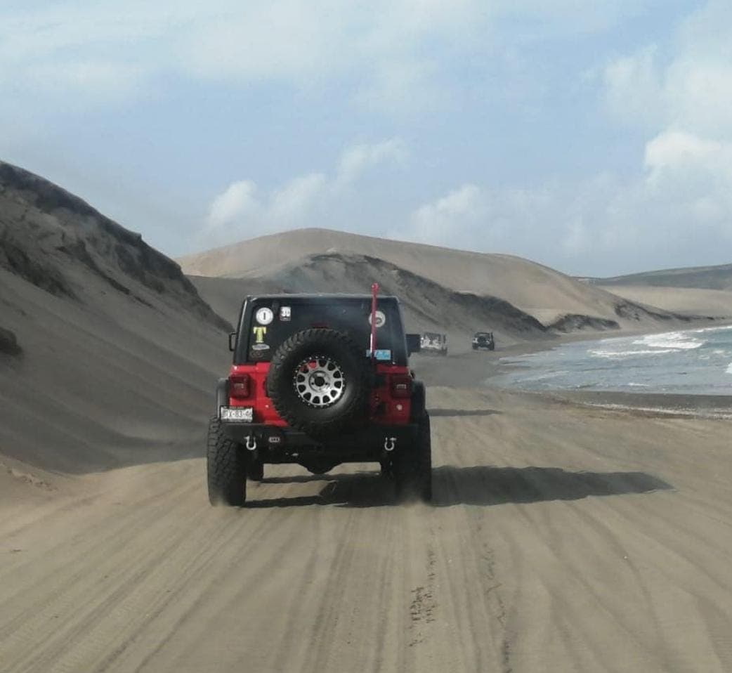 Jeep Wrangler roja avanzando por las dunas junto al mar